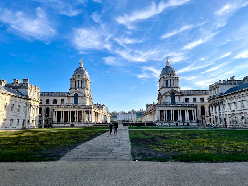 A spacious urban park in Royal Greenwich, showing well-maintained garden beds and neatly trimmed grass, with a large, historic white stone building featuring classical architecture, columns, and domed